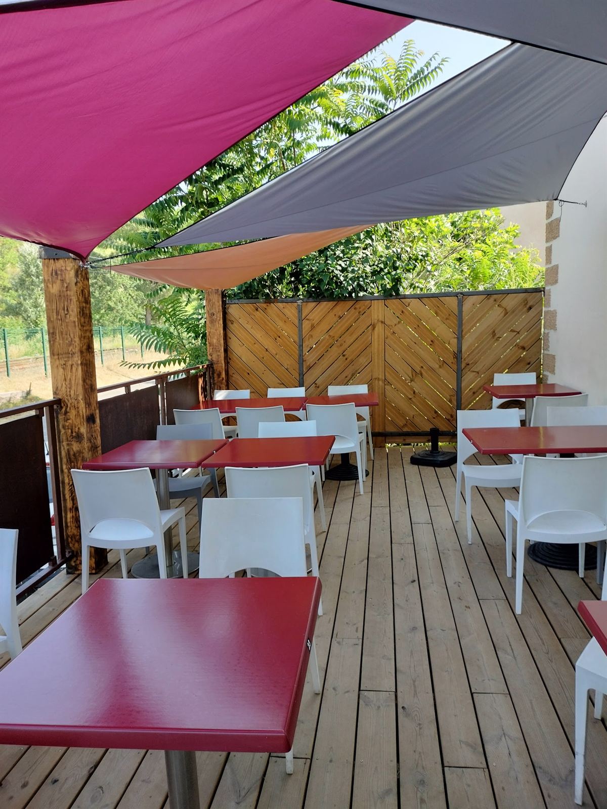 La terrasse en bois, tables rouges et voiles d'ombrage